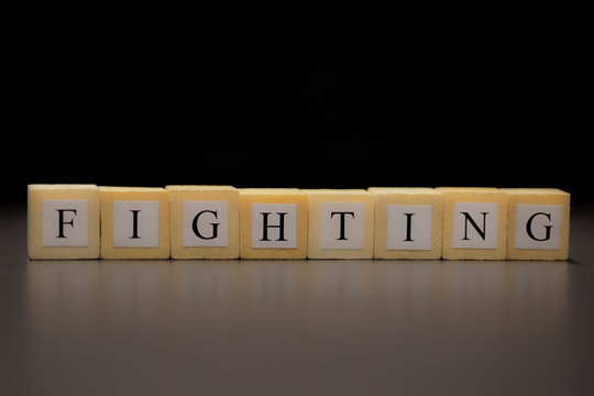 The word FIGHTING written on wooden cubes isolated on a black background..