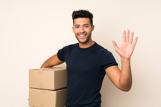 Young handsome man over isolated background holding a box to move it to another site and saluting