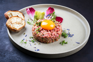 Gourmet Tartar roh vom Rinderfilet mit Eigelb und gegrilltem Baguette als closeup auf einem Modern Design Teller