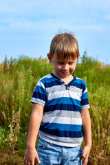 Little boy 5-6 years old in a T-shirt on a green meadow in the summer.