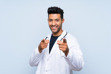 Young doctor man over isolated blue wall points finger at you with a confident expression