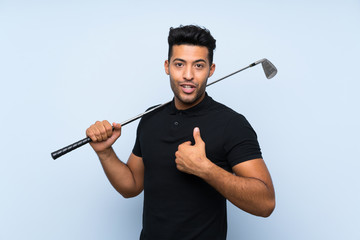 Handsome young man playing golf over isolated blue background with surprise facial expression