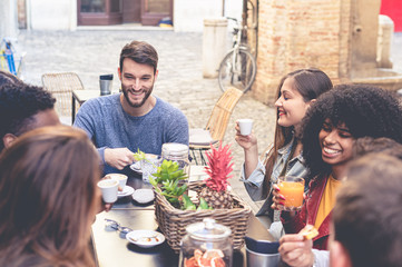 Group of young multiracial people having breakfast in an outdoor coffee shop. Students of different...