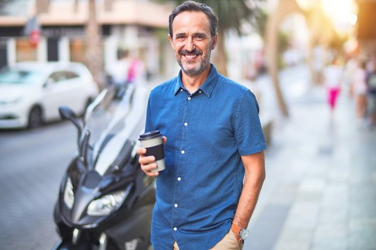 Middle age handsome man standing on the street drinking take away coffee smiling