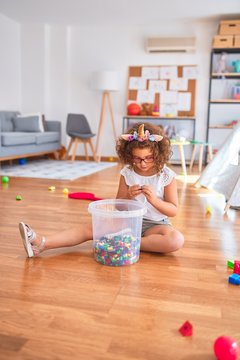 Beautiful toddler wearing glasses and unicorn diadem sitting on the floor playing with building blocks at kindergarten