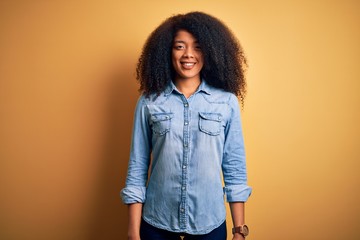 Young beautiful african american woman with afro hair standing over yellow isolated background with a happy and cool smile on face. Lucky person.