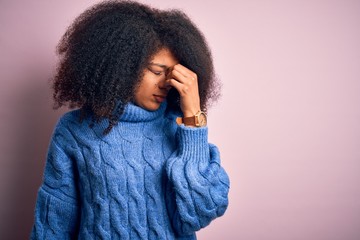 Young beautiful african american woman with afro hair wearing winter sweater over pink background tired rubbing nose and eyes feeling fatigue and headache. Stress and frustration concept.