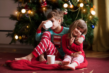 Two kids drinking cocoa near Christmas tree at home. Hygge. Happy family on Christmas holiday.