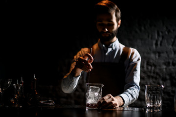 Male bartender stirring an ice cubes in the glass with special spoon to the glass