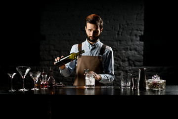 Professional bartender pouring a alcoholic drink from the bottle to a steel jigger