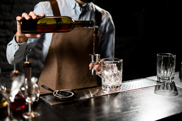Male bartender pouring a alcoholic drink from the bottle to a steel jigger