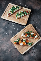 4 bruschetta with pumpkin, feta, olives, butter, avocado, sun-dried tomatoes and arugula on a brown background