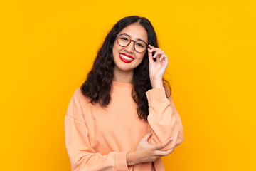 Spanish Chinese woman over isolated yellow background with glasses and happy