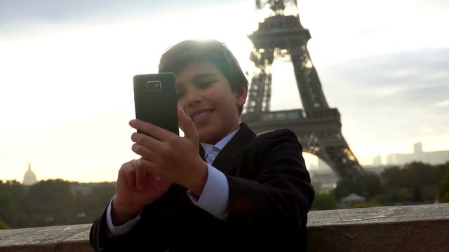 Beautiful teenager boy is making a photo on the phone on the background of the Eiffel tower, Paris, France