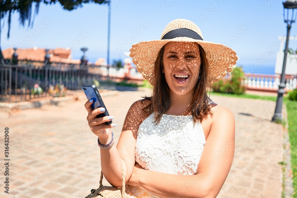 Wall mural young beautiful woman smiling happy walking on city streets on a sunny day of summer using smartphon