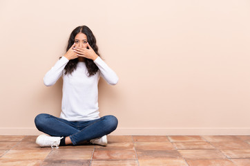 Young woman sitting on the floor covering mouth with hands