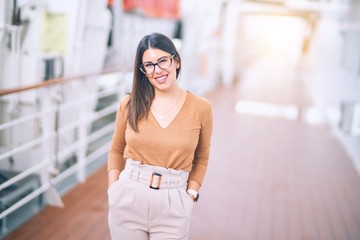 Young beautiful woman on vacation smiling happy and confident. Standing on a deck of ship with smile on face doing a cruise