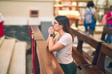 Young beautiful woman praying on her knees in a bench at church