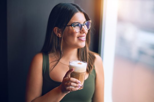 Young beautiful woman on vacation smiling happy and confident. Standing on a deck of ship with smile on drinking coffee face doing a cruise