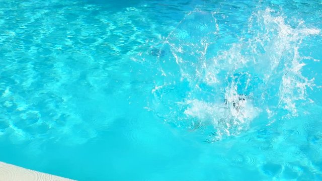 Boy in swimming gogles is jumping into the pool. Splashes fly away