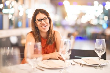 Young beautiful girl smiling happy and confident sitting on chair at restaurant. Relaxing with a smile on face