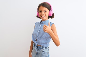 Beautiful child girl listening to music using headphones over isolated white background doing happy thumbs up gesture with hand. Approving expression looking at the camera with showing success.