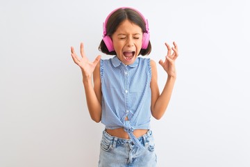 Beautiful child girl listening to music using headphones over isolated white background celebrating mad and crazy for success with arms raised and closed eyes screaming excited. Winner concept