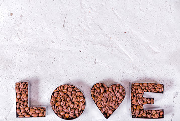 The inscription love is laid out with coffee beans using metal shapes on a concrete background.
