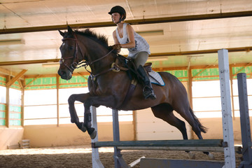 Female rider jumping over an oxer during riding lessons in indoor arena