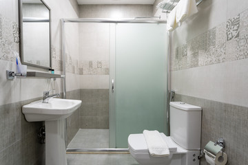 Bathroom with glazed shower, mirror over the sink, towel and toilet.