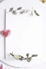 Background with copy space blank on white table with glitter heart, eucalyptus branch, flowers and leafs. White paper top view, flat lay, minimal style. Moke up card.