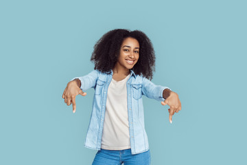 Freestyle. African girl standing isolated on gray pointing down copy space smiling happy