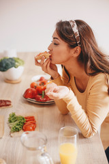 Obraz na płótnie Canvas A woman eating a sandwich over the kitchen counter.
