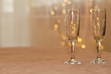 Two empty wine glasses on a surface on right background of white translucent curtains with lights of a garland the day.