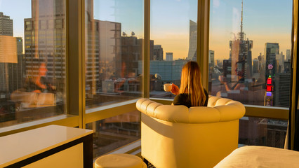 CLOSE UP: Woman having a cup of tea while observing the evening cityscape.