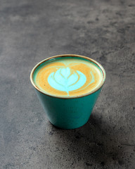 Close up of turquoise colored capuccino with latte art on gray background