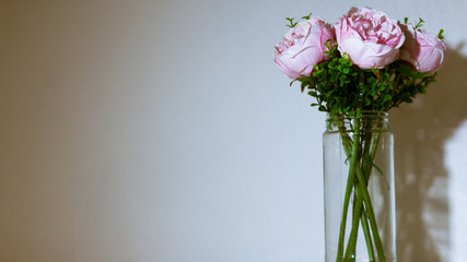 Ramo de flores artificiales en un florero de vidrio. Luz directa blanca sobre el ramo y fondo de pared blanca. Ramo de flores aislado. 