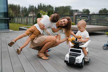 Young mother playing and having fun with her baby boy son brothers in a green garden with cars - Family values warm color summer scene - Eastern European Latvia Riga