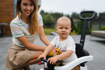 Fototapeta premium Young mother playing and having fun with her baby boy son brothers in a green garden with cars - Family values warm color summer scene - Eastern European Latvia Riga