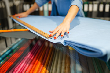 Woman measures the fabric in textile store - obrazy, fototapety, plakaty