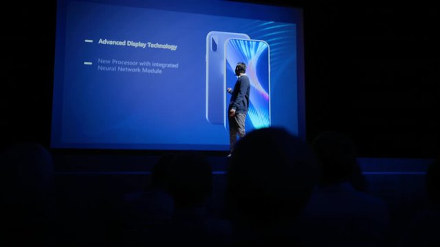 Live Event with Brand New Products Launch: Keynote Speaker Reveals Smartphone Device to Audience. Movie Theater Screen Shows Mock-up Touch Screen Mobile Phone with High-End Features and Top Highlights