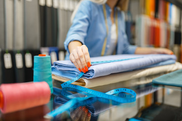 Female seller measures fabric in textile store