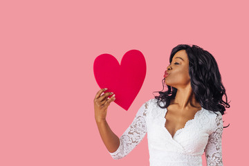 Profile portrait of young happy woman holding pink heart and blowing a kiss, valentineÕs day love