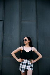 Sexy girl near a dark wall in a T-shirt, sunglasses and short shorts