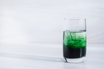 Chlorophyll in glass of water on white wooden background. Copy space, sunlight.