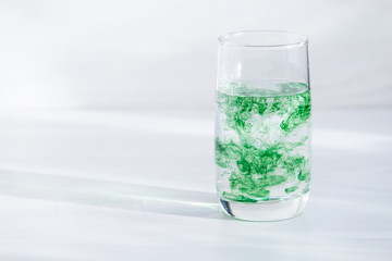 Chlorophyll in glass of water on white wooden background. Copy space, sunlight.
