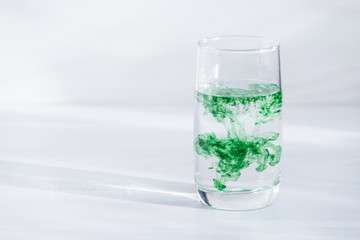 Chlorophyll in glass of water on white wooden background. Copy space, sunlight.