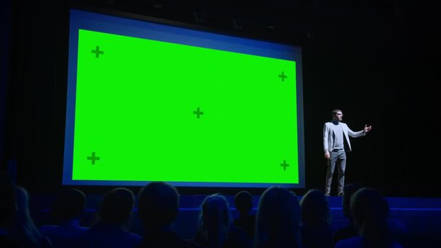 Keynote Speaker Does Presentation of New Product to the Audience, Behind Him Movie Theater with Green Screen, Mock-up, Chroma Key. Business Conference Live Event or Device Reveal