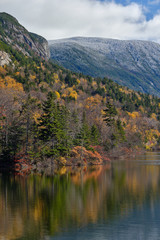 Fototapeta na wymiar Autumn colors along the shore of Echo lake in New Hampshire with snow and frost on he tops of the White Mountains
