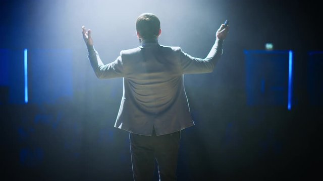 Back View of Successful Motivational Speaker, Talking about Happiness, Self, Success, Empowerment, Efficiency, Health, and How to Be More Productive. Large Conference Hall with Cinematographic Light